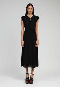 Robe noire mi-longue avec des manches courtes et structurées, un col rond et un détail en fente à l'avant. Fabriquée en tissu léger avec une silhouette fluide.