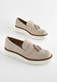 Beige nahka loaferit, joissa on tupsukoriste, paksu valkoinen ulkopohja ja ruskea välikerros, sileä pinta ja pyöristetty kärki.