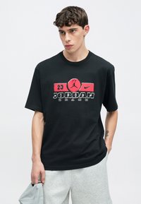 Μαύρο βαμβακερό t-shirt με πολύχρωμο γραφικό που αναγράφει "JORDAN" και τον αριθμό "23" μπροστά. Κοντά μανίκια και σχέδιο με στρογγυλή λαιμόκοψη.
