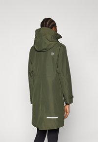 Olivgrüne wasserdichte Jacke mit Kapuze, lang geschnitten, verstellbaren Manschetten und einem weißen reflektierenden Akzent am Saum. Logo auf der Rückseite.