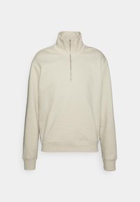Sudadera beige con un cuello alto, media cremallera en el frente y puños acanalados. Fabricada con un tejido suave, presenta un branding mínimo en el pecho.