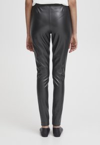 Leggings en cuir noir avec une texture lisse, taille haute et design ajusté, s'étendant jusqu'aux chevilles. Couleur unie, sans motifs visibles.