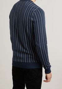 Námořnický svetr s vertikálními bílými pruhy, žebrovanými manžetami a lemem a kulatým výstřihem, vyrobený z měkké strukturované látky.