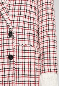 Giacca in misto lana con un motivo a quadri rosa e bianco, dettagli in rosso e nero, grandi bottoni neri e un polso bianco testurizzato.