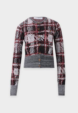 Vrouw draagt een rode en zwarte geruite cropped cardigan, glanzende zwarte knielange rok, zwarte laarzen met hak en houdt een zwarte handtas vast.