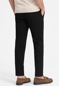 Schwarze Hose mit maßgeschneidertem Schnitt, mit glatter Textur und Seitentaschen. Kombiniert mit braunen Wildleder-Slippern.