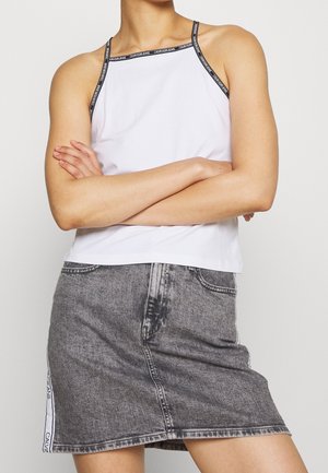 Witte tanktop met dunne zwarte bandjes met het logo "Calvin Klein Jeans", gecombineerd met een grijze denim rok met witte zijdetails.