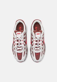 Nike tenisky s bílou síťovinou, červenými akcenty a vyšitými detaily. Mají silné bílé tkaničky a polstrovanou vložku. Je viditelné červené logo.