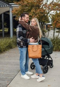 Pár v parku, nosící hnědý manšestrový kabát a kostkovanou košili; světle modré džíny; světle hnědá kožená taška; černý kočárek se zelenou látkou.