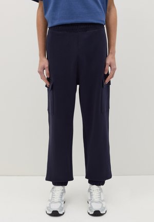 Pantalones de chándal azul marino con cintura elástica, puños acanalados y dos bolsillos laterales. Combinados con zapatillas blancas y grises.