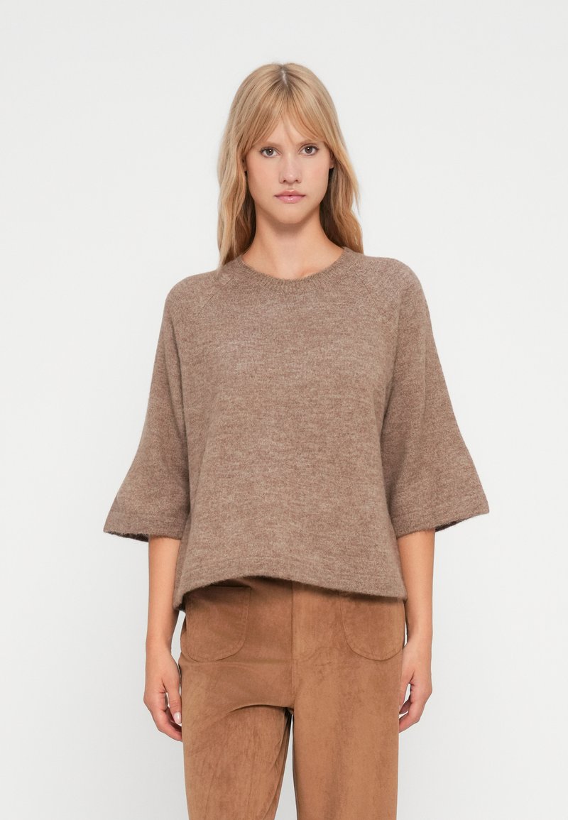 Maglione marrone lavorato a maglia con maniche corte e scollatura arrotondata. Tessuto morbido e vestibilità rilassata, abbinato a pantaloni beige simili alla pelle scamosciata.
