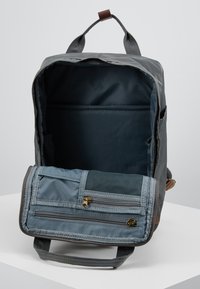 Sac à dos en tissu gris avec une poche avant zippée, des bretelles ajustables et un intérieur spacieux. Comprend un panneau en maille et des accents en zipper doré.