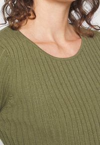 Haut en maille côtelée vert olive avec un large décolleté en U, présentant un tissu texturé et une silhouette ajustée mettant en valeur les lignes verticales.