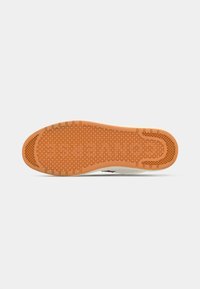Shoe sole with textured orange rubber, featuring a pattern of small circles and a smooth section near the heel, set against a white background.