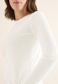 Langsleeve top van zachte, ribbelige witte stof. Heeft een ronde halslijn en een gestructureerd oppervlak met subtiele verticale lijnen voor visuele interesse.