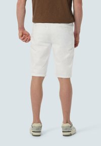 Weiße Baumwollshorts mit geradem Schnitt, Gesäßtaschen und umgeschlagenem Saum, kombiniert mit grauen Turnschuhen auf einem hellblauen Hintergrund.