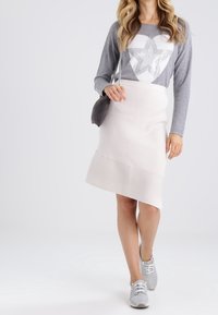 Grijze lange mouwen top met een sterrenafbeelding, gecombineerd met een crèmekleurige asymmetrische rok met ribbelstructuur en een subtiel kleurcontrast, gedragen met grijze sneakers.