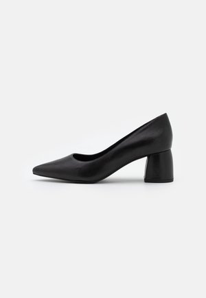 Zapato de tacón negro de cuero con punta afilada y tacón bloque medio; textura suave y detalles mínimos, que proporcionan una silueta elegante.