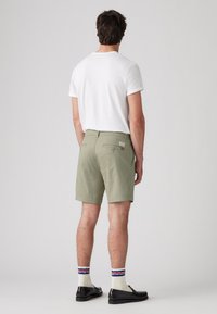 Pantaloni scurți de culoare verde deschis, cu o croială ajustată, două buzunare la spate și o etichetă de marcă; asortați cu un tricou alb și mocasini negri.