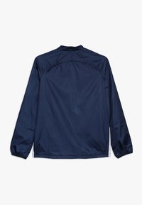 Námořnická modrá lehká bunda vyrobená z hladkého, voděodolného materiálu. Má dlouhé rukávy, vysoký límec a elastické manžety.