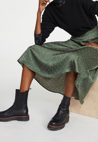 Grøn mønstret satin nederdel med et flydende design, parret med sorte læder ankelstøvler med elastiske sider og en tekstureret sål.