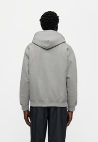 Γκρι φούτερ με κουκούλα από μαλακό υλικό, διαθέτει μεγάλη κουκούλα, χαλαρή εφαρμογή και ριμπ μανσέτες. Απλός σχεδιασμός χωρίς σχέδια ή διακοσμητικά στοιχεία.