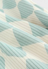 Mint zöld és világos krém színű mintás szövet, váltakozó sima és bordázott textúrákkal, nagy absztrakt formákkal.