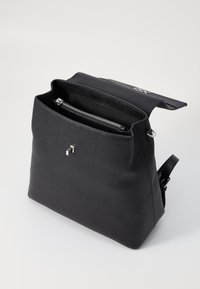 Sac à main noir avec un extérieur texturé, ouverture en haut et forme rectangulaire. Comprend une poche zippée argentée à l'intérieur et un logo discret.