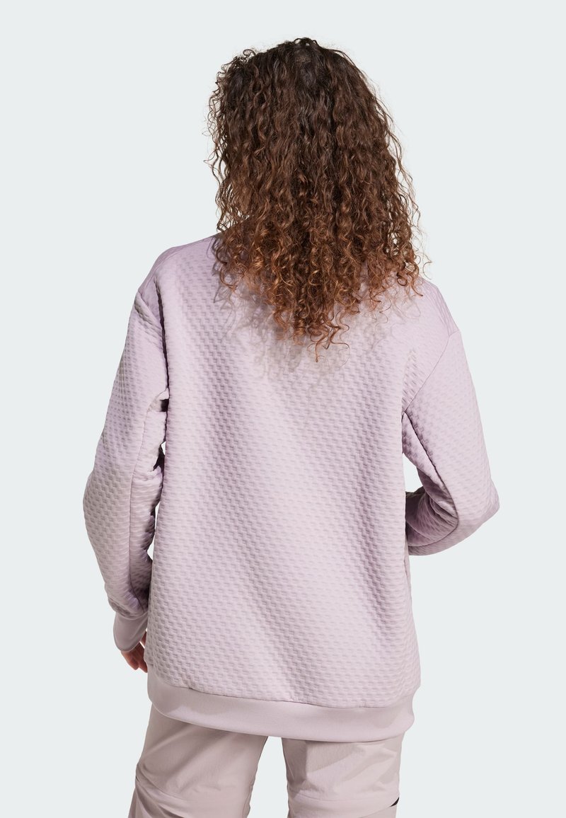 Ljuslila sweatshirt med texturerat mönster, sänkta axlar, ribbade muddar och nederkant. Utsikt från baksidan som visar lockigt hår.