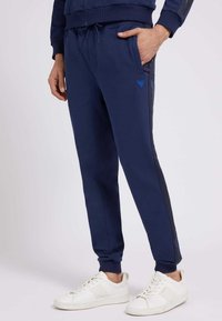 Navy blue athletic pants made of soft fabric, featuring a slim fit, elastic waistband with drawstring, and contrasting black side stripes.