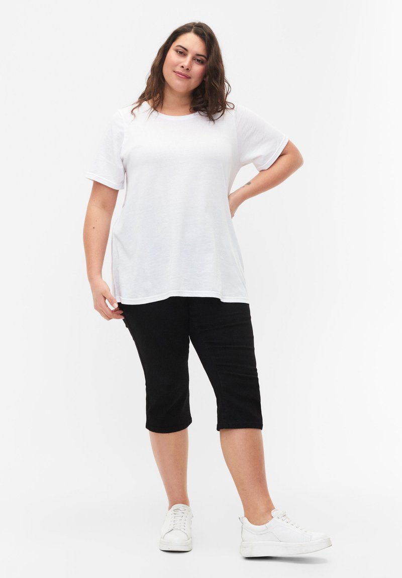 Camiseta blanca de manga corta combinada con pantalones negros a la altura de la rodilla y zapatillas blancas. Diseño sencillo, tejido suave, ajuste relajado.