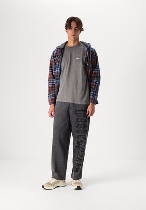 Plaid flannel jacket in red and blue, gray t-shirt with logo, gray baggy pants with black text, and beige athletic shoes.