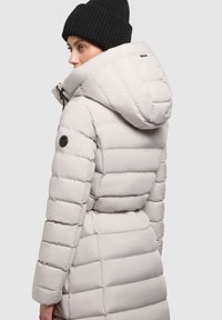 Lichtgrijze, puffy jas met een aangesnoerde taille, grote capuchon en zwart logo-opdruk op de mouw; beschikt over horizontale stiksels en een gladde textuur.