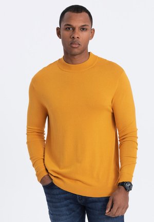 Mustard yellow knit sweater with ribbed neckline and cuffs, worn over dark jeans. Features a close-fitting design and smooth texture.