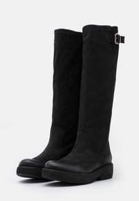 Bottes noires montant jusqu'aux genoux en cuir texturé avec un bout lisse, un accent de boucle latérale et une semelle plateforme basse et robuste.