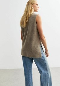 Beige ärmlös stickad tröja med ribbad textur, sidofickor, ihop med lösa ljusblå jeans. Mjukt tyg, avslappnad passform.