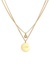 Collana in metallo dorato con due catene; presenta un pendente circolare con un design inciso e un piccolo ciondolo decorativo sopra.