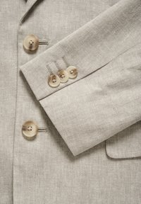 Hellbeige Leinenblazer mit strukturiertem Finish, ausgestattet mit vier großen, runden Knöpfen in einer kontrastierenden Farbe und kontrastierenden Nahtstichen.