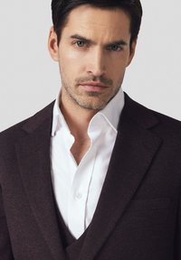 Ciemnoczerwona marynarka w garniturze na białej koszuli, z klapami notch, teksturowanym materiałem i dopasowanym krojem. Widoczne czyste, ostre krawędzie kołnierzyka.