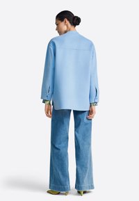 Lahek modro nebo oversize srajca z dolgimi rokavi in stranskimi razporki, kombinirana z širokimi jeans hlačami. Obleko dopolnjujejo petke z zelenim poudarkom.