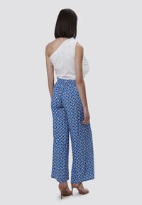 Witte off-shoulder top gecombineerd met blauwe wijde broek met geometrische patronen. Soepele stoffen en een elastische tailleband.