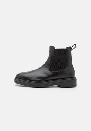 Botas de tobillo de cuero negro con paneles laterales elásticos, punta redonda, tira de agarre y una suela de goma resistente. Textura suave con un diseño minimalista.