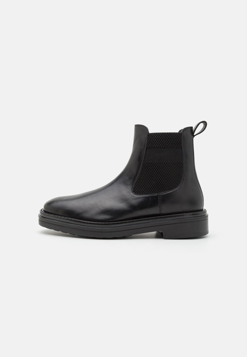 Botas de tornozelo em couro preto com painéis laterais elásticos, bico arredondado, alça para puxar e sola de borracha robusta. Textura suave com detalhes minimalistas.