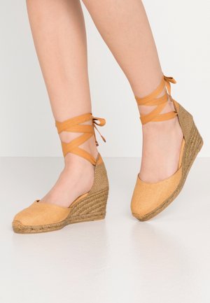 Bottes compensées beiges avec une semelle en jute texturée. Présentent des lanières en tissu croisées autour de la cheville et un design à bout rond.