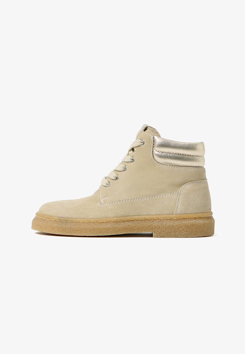 Bottine beige en daim avec semelle en caoutchouc marron clair, lacets à l'avant, et détail de col rembourré métallique vue de profil.