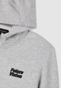 Felpa con cappuccio grigia realizzata in tessuto morbido, con un logo nero "Future Vision". Il design include una tasca a marsupio e bordi ribattuti.