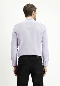 Camicia a maniche lunghe di colore viola chiaro con colletto, design aderente, polsini con bottone e texture tonale, abbinata a pantaloni neri.