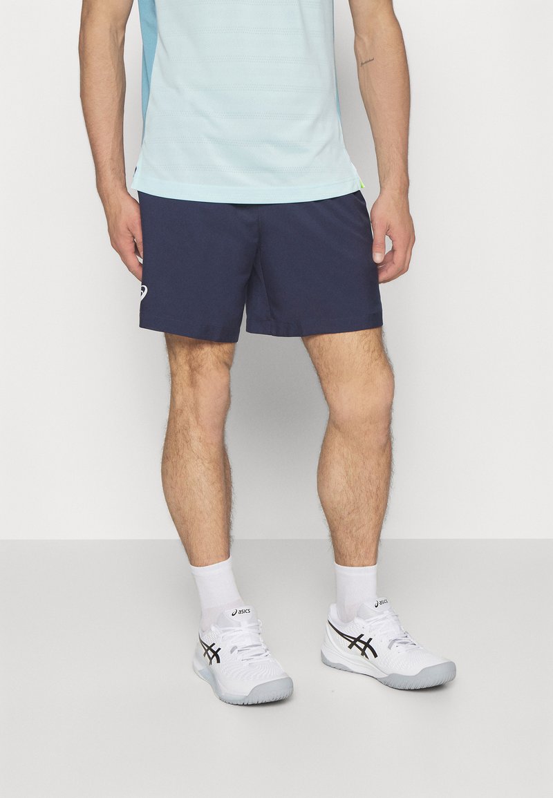 Pantalones cortos navy con cinturilla elástica, combinados con una camiseta deportiva de manga corta en azul claro. Zapatillas deportivas blancas con detalles en negro.