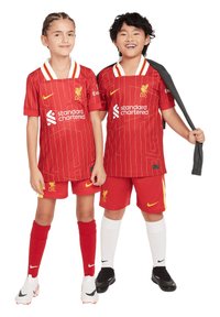 Maglie rosse del Liverpool FC con accenti bianchi, caratterizzate da un design a righe. I giocatori indossano pantaloni rossi, calze rosse e calze bianche, con il marchio Nike.