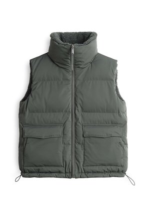 Gilet matelassé en vert foncé, avec un col haut, une fermeture éclair et deux poches avant avec des détails à rabat. Doublure intérieure douce.